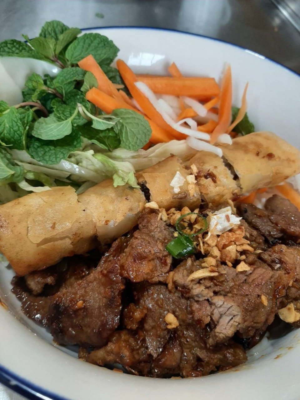 Grilled beef on noodles with spring rolls and vegetables.